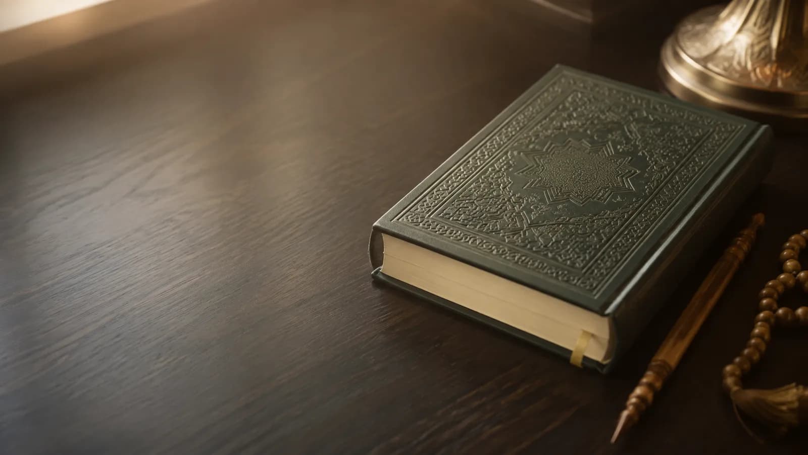 A closed embossed Quran on a dark wooden desk with a wooden reading pointer and prayer beads beside it