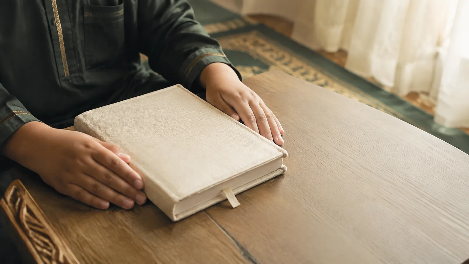 A child's hands resting on a closed Quran on a low wooden table