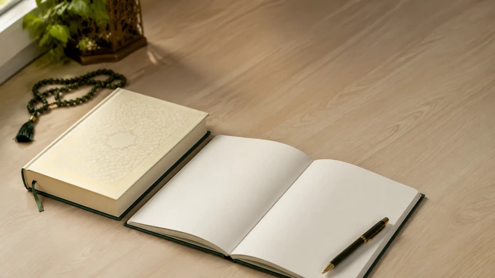 A closed Quran beside an open blank notebook and pen on a desk, with prayer beads and a lantern